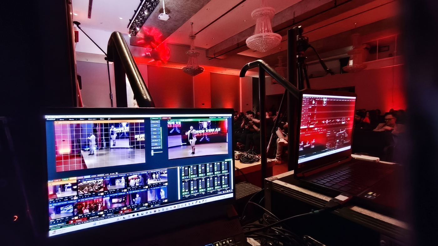 Mesa de corte com monitores exibindo a transmissão de um evento com iluminação vermelha