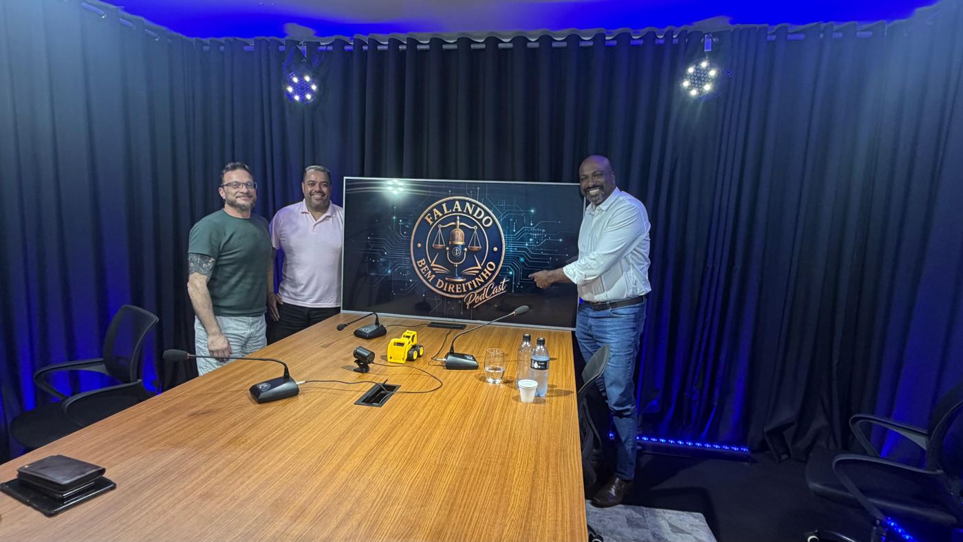 Três convidados no estúdio NaSuaTela ao lado do telão de um podcast